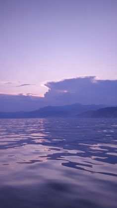 the sun is setting over the water with mountains in the distance and clouds in the sky