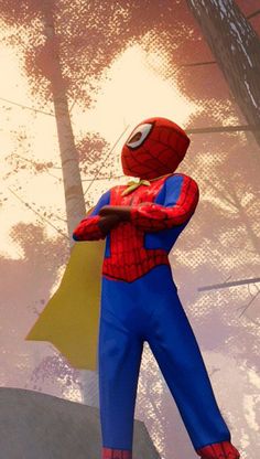 a man dressed as spider - man standing in front of some trees and looking at his cell phone