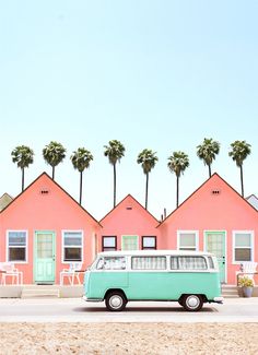 a blue and white van parked in front of pink houses with palm trees on the roof