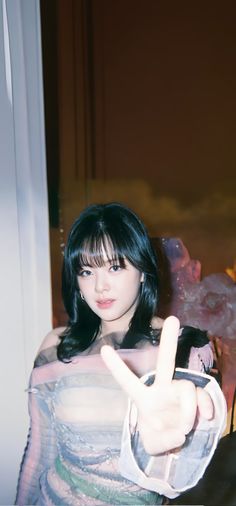 a woman with black hair and bangs making the peace sign while sitting in a chair