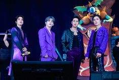 three men in purple outfits standing on stage with one holding a microphone and the other looking at something