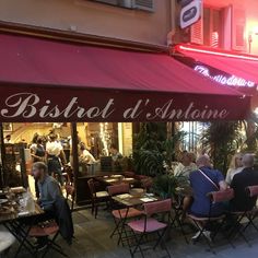 people are sitting at tables outside in front of a restaurant with red awnings