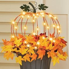 a pumpkin shaped planter filled with leaves and fairy lights on the outside of a house