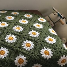 a crocheted blanket with white and yellow flowers on it next to a stuffed animal