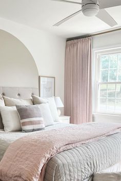 a large bed sitting under a window next to a white ceiling fan in a bedroom