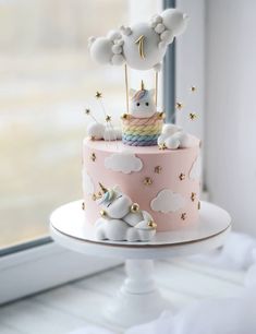 there is a pink cake with white clouds and a small unicorn on top that has gold stars