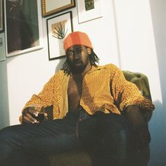 a man sitting in a chair holding a drink and looking at his cell phone while wearing an orange hat