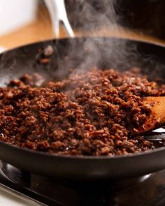 a frying pan filled with food cooking on top of a stove burner next to a wooden spoon