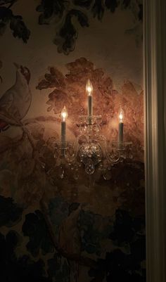 three candles are lit on a wall in a room with floral designs and birds painted on the walls