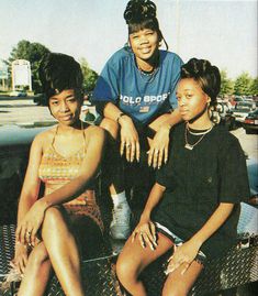 three young women sitting on the back of a car in front of a parking lot