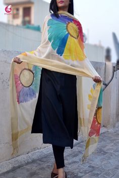 a woman is standing on the sidewalk holding a colorful shawl over her head and looking off into the distance