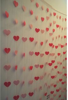 paper hearts are hanging on the wall in front of a white backdrop with pink and red decorations