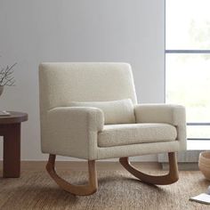 a white rocking chair sitting on top of a hard wood floor next to a window