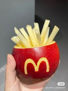 a hand holding a red apple with french fries in the shape of a mcdonald's logo