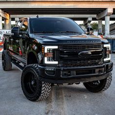 a large black truck parked in front of a parking garage with its lights on and tires off