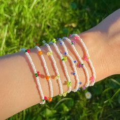 a person's arm with bracelets on it and flowers in the grass behind them