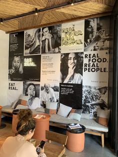 a woman sitting at a table in front of a wall with posters on it