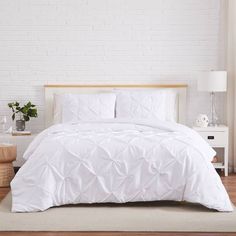 a bed with white comforter and pillows in a room next to a brick wall