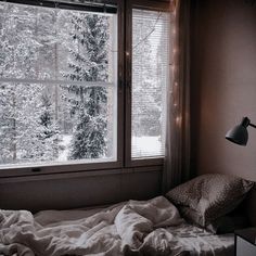 an unmade bed sitting in front of a window with lights on the windowsill