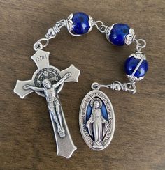 "This beautiful Chaplet is made of 10mm blue tone beads, stainless steel wire, 1\" miraculous medal and 2 inches crucifix." Adjustable Rosary With Miraculous Medal And Crucifix, Adjustable Blue Rosary With Miraculous Medal, Adjustable Blue Rosary With 8mm Beads, Blue Rosary With 8mm Beads And Crucifix, Adjustable Blue Rosary Bracelet With Cross, Blue Rosary With 8mm Beads In Cross Shape, Adjustable Blue Cross-shaped Jewelry, Blue Cross Jewelry With 8mm Beads, Blue Cross-shaped Jewelry With 8mm Beads