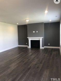 an empty living room with gray walls and wood flooring in the center is a fireplace