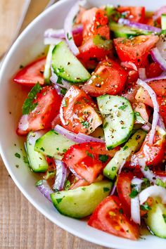 a white bowl filled with cucumber and tomato salad on top of a wooden table