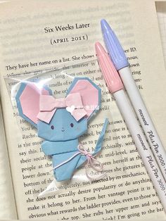 two pink and blue paper animals sitting on top of an open book next to each other