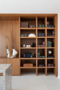 a wooden bookcase filled with lots of books next to a white vase on top of a table