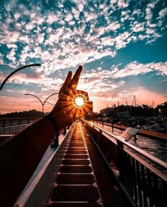 a person holding their hand up with the sun setting in the sky behind them,