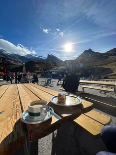 two coffee cups on a picnic table with the sun shining over mountains in the background