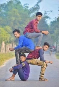 four young men are standing on one another in the middle of an empty road with trees behind them