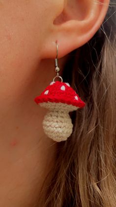 a woman wearing red and white crochet earrings with a mushroom on it's ear