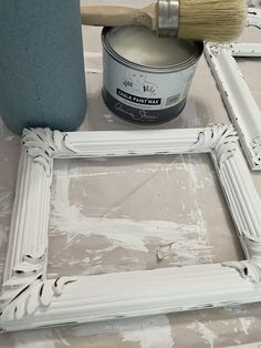 a paint can and brush sitting on top of a table next to a white frame