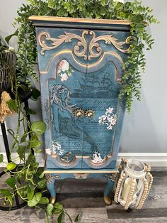 a blue cabinet with flowers on it next to a potted plant and other items