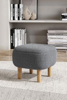 a grey ottoman sitting on top of a white rug in front of a book shelf