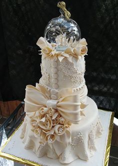 a three tiered white wedding cake with flowers on top and a glass dome in the middle