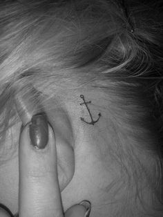 a woman with a small anchor tattoo on her ear and behind her ear is the words behind her ear