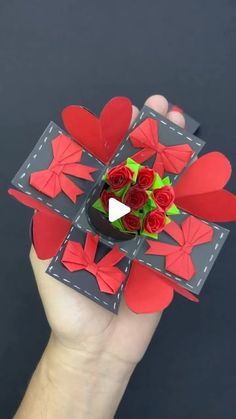 someone is holding up a card with red paper flowers and heart shapes on the front