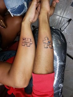 two people with matching tattoos on their arms holding each other's hands and one has a piece of the same puzzle