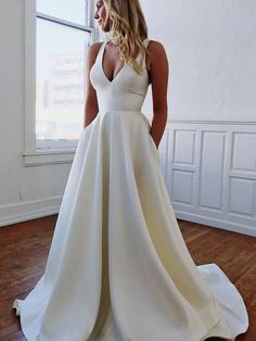 a woman standing in front of a window wearing a white wedding dress with deep v - neck