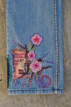 a blue jean jacket with pink flowers on the side and a notepad attached to it