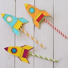 three colorful paper rockets are sitting on a white wooden surface with candy canes in the shape of rocket ships