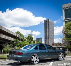 a blue car parked in a parking lot with tall buildings in the backgroud