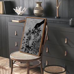 a chair sitting in front of a painting on top of a wooden table next to a vase