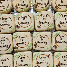 some cookies with writing on them are sitting on a cooling rack and one cookie has the words love is brewing written on it