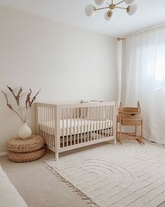 a white crib in the corner of a room next to a window with sheer curtains