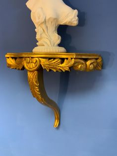 a golden shelf with a white busturine on it's top and a blue wall in the background