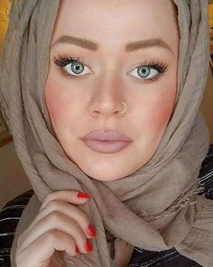 a woman with blue eyes wearing a hijab and nose piercing is posing for the camera