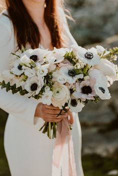 a woman holding a bouquet of white and black flowers on her wedding day in front of some rocks