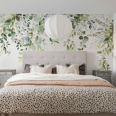 a large bed sitting under a white light next to a wall with green leaves on it